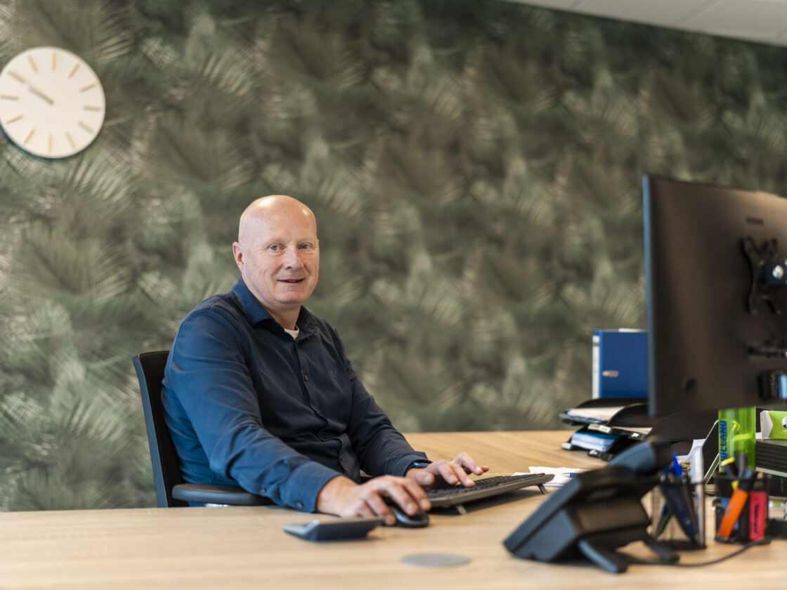 Wex Holland medewerker van Team Global achter zijn bureau lachend in de camera