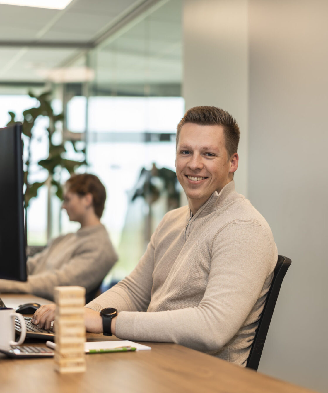 Medewerker Wex Holland als procesmanager lachend naar de camera achter zijn bureau