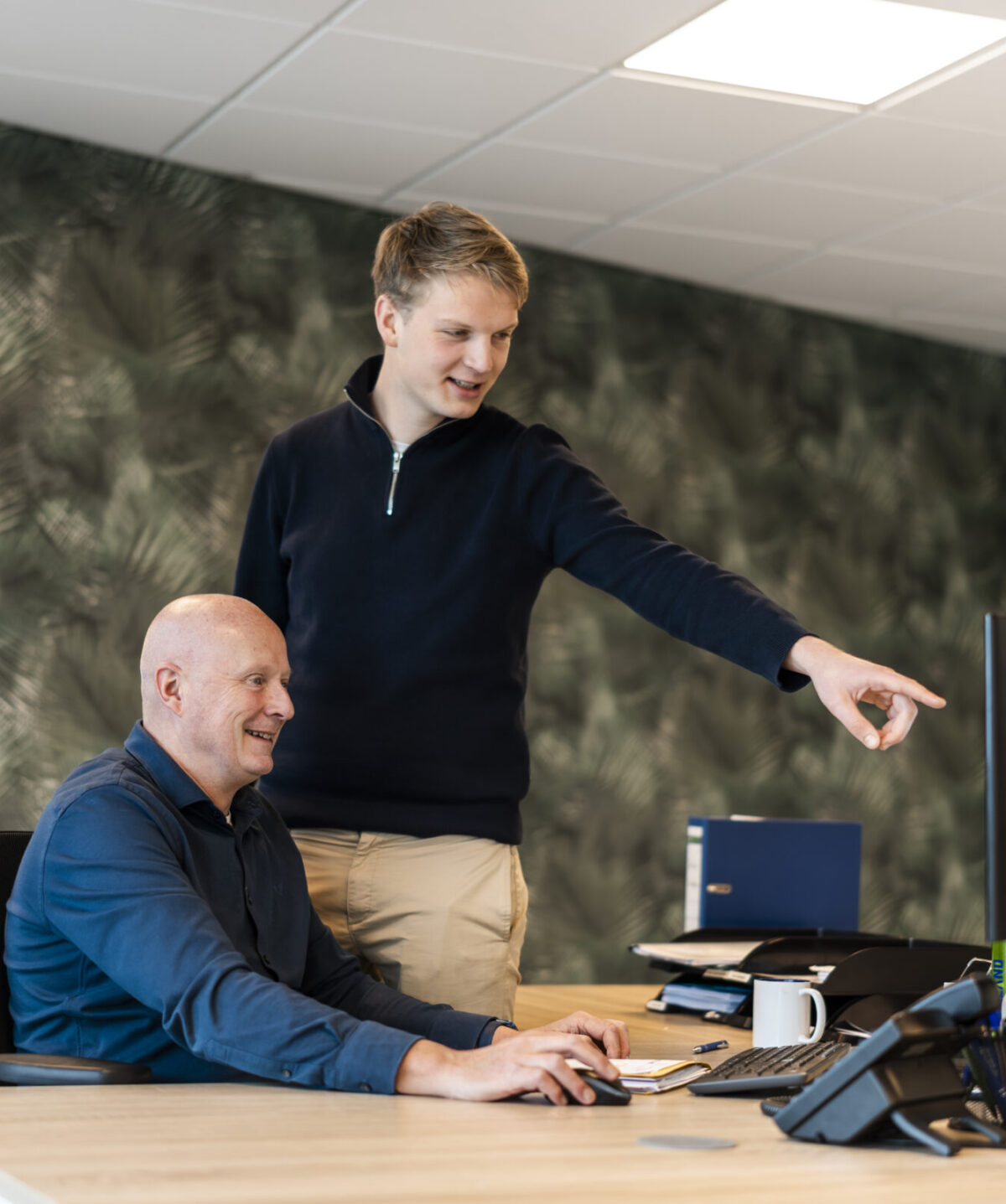 Medewerkers Wex Holland uit team Global lachend en wijzend naar het beeldscherm van achter een bureau