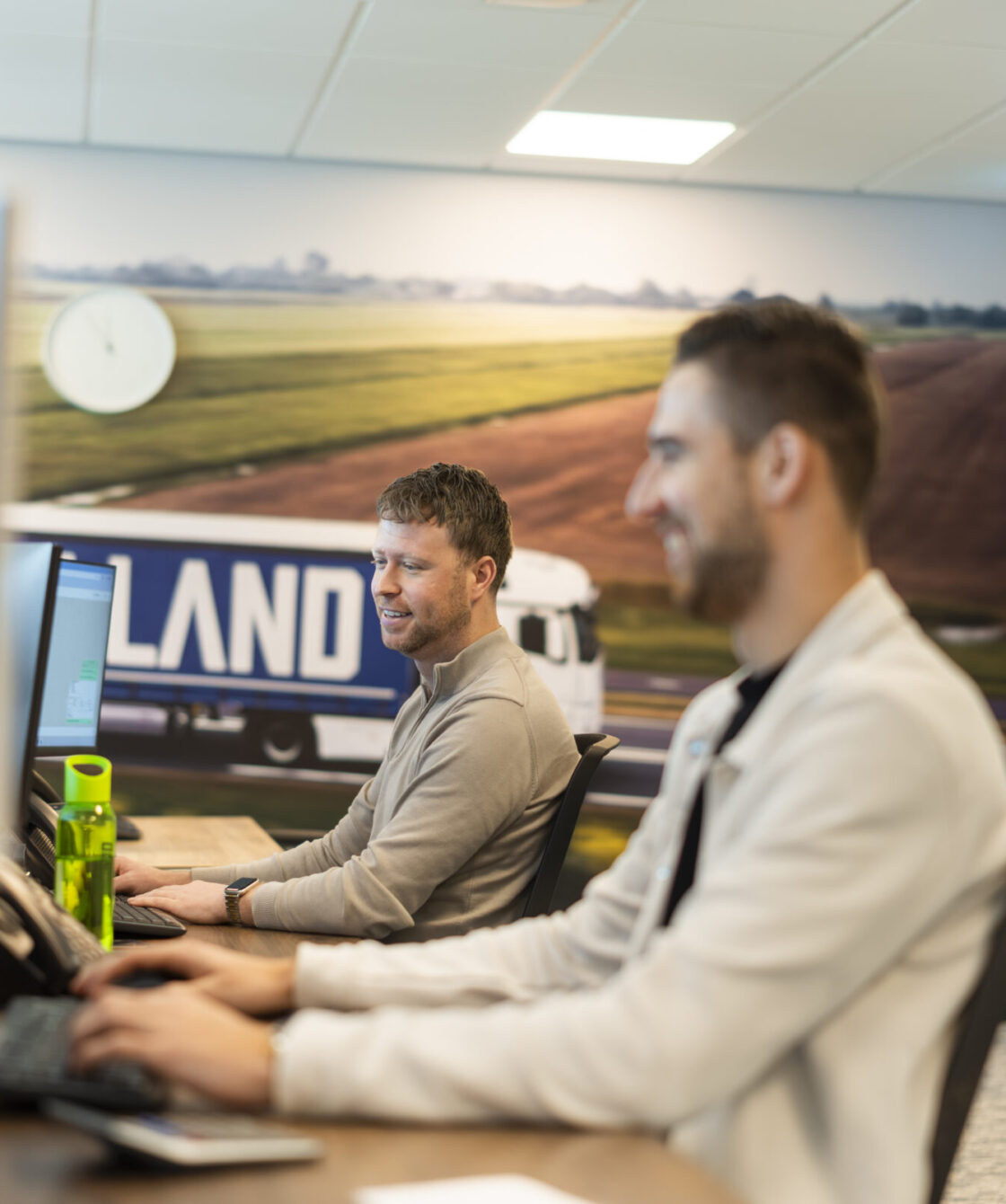 Medewerkers Wex Holland als transportplanner achter een bureau lachend en kijkend naar een beeldscherm