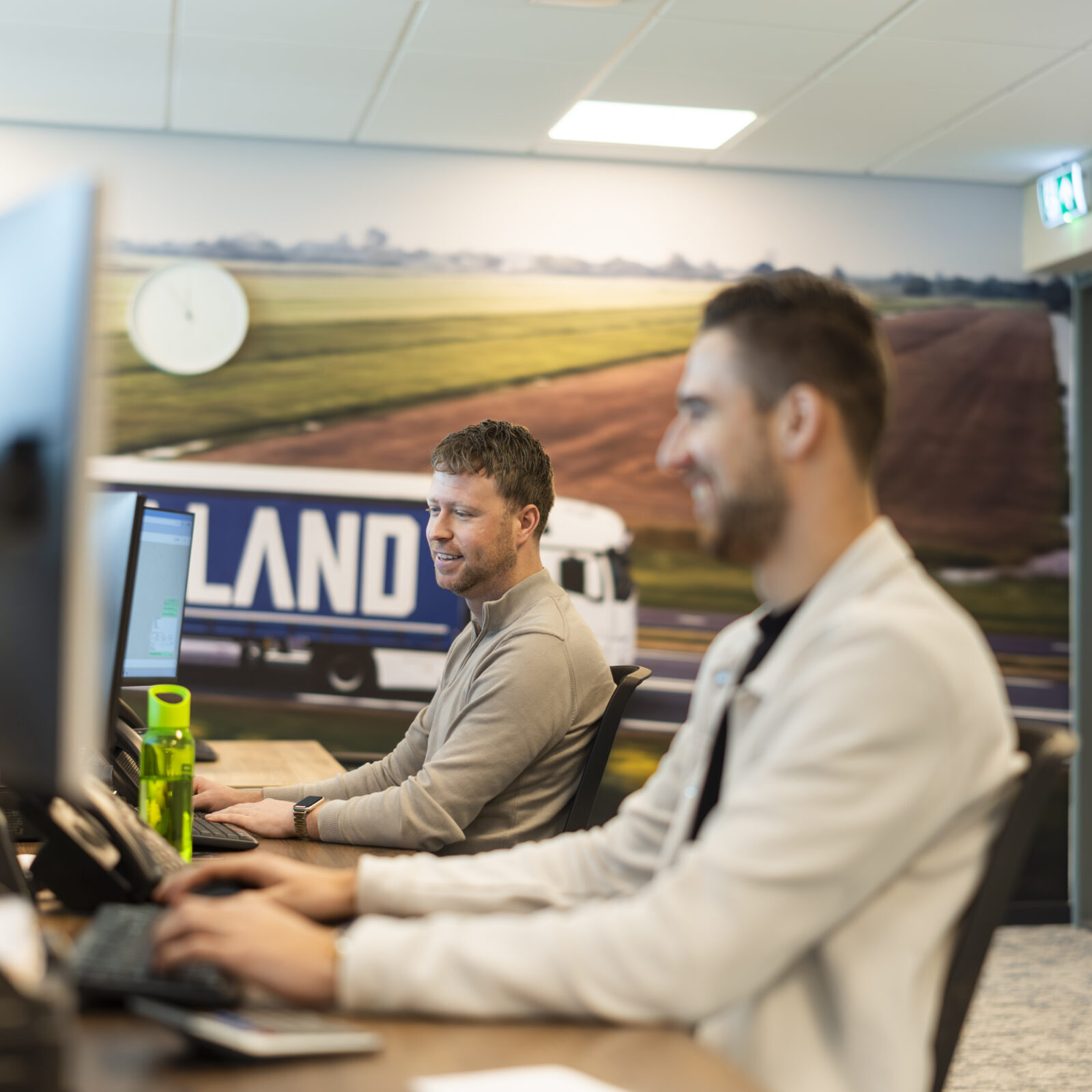 Medewerkers Wex Holland als transportplanner achter een bureau lachend en kijkend naar een beeldscherm